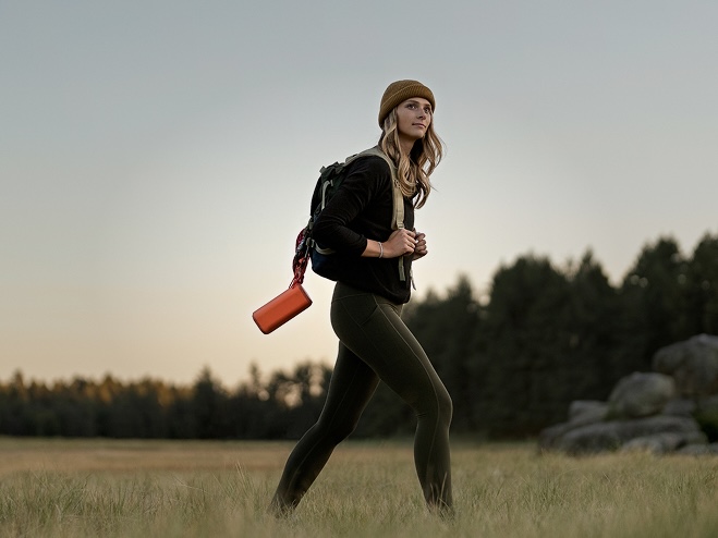 A woman hiking outdoors, carrying a bag with a SONY speaker hanging from it